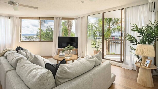 A modern living room with a large sofa, a round coffee table, and a TV. - Palms on Gold Riverfront Haven by Gold Coast Beach (Surfers Paradise)