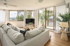 A modern living room with a large sofa, a round coffee table, and a TV. - Palms on Gold Riverfront Haven by Gold Coast Beach (Surfers Paradise)