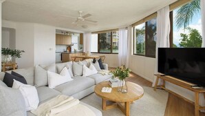 A modern living room with a large sofa, a coffee table, and a TV. - Palms on Gold Riverfront Haven by Gold Coast Beach (Surfers Paradise)
