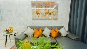A modern living room with a grey sofa, orange and grey cushions, a glass coffee table, and a framed artwork of horses on the wall. - Premium One Bedroom Apartment at KASS (Accra)