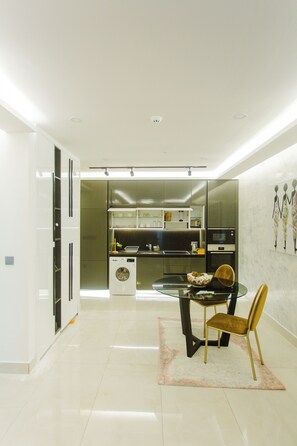 A modern kitchen with a built-in oven, a washing machine, and a dining area with a glass table and chairs. - Premium One Bedroom Apartment at KASS (Accra)