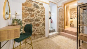 A hallway with a stone wall, a wooden desk with a green chair, and a mirror. - DP Homes Exarcheia 1B - Central Stone Apt near Metro & Museum (Athina)