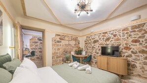 A hotel room with a bed, a TV, a desk with a chair, and a stone wall. - DP Homes Exarcheia 1B - Central Stone Apt near Metro & Museum (Athina)