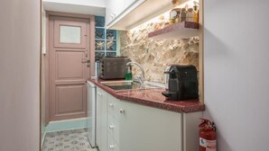 A compact kitchen with a stone backsplash, a coffee maker, and a fire extinguisher. - DP Homes Exarcheia 1B - Central Stone Apt near Metro & Museum (Athina)