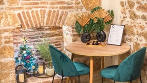 A rustic stone wall, a small Christmas tree, teal chairs, a round wooden table with a menu, and a decorative plant arrangement. - DP Homes Exarcheia 1B - Central Stone Apt near Metro & Museum (Athina)
