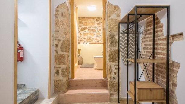 A staircase leading to a bathroom with a stone wall, a wooden bench, and a metal shelf unit. - DP Homes Exarcheia 1B - Central Stone Apt near Metro & Museum (Athina)