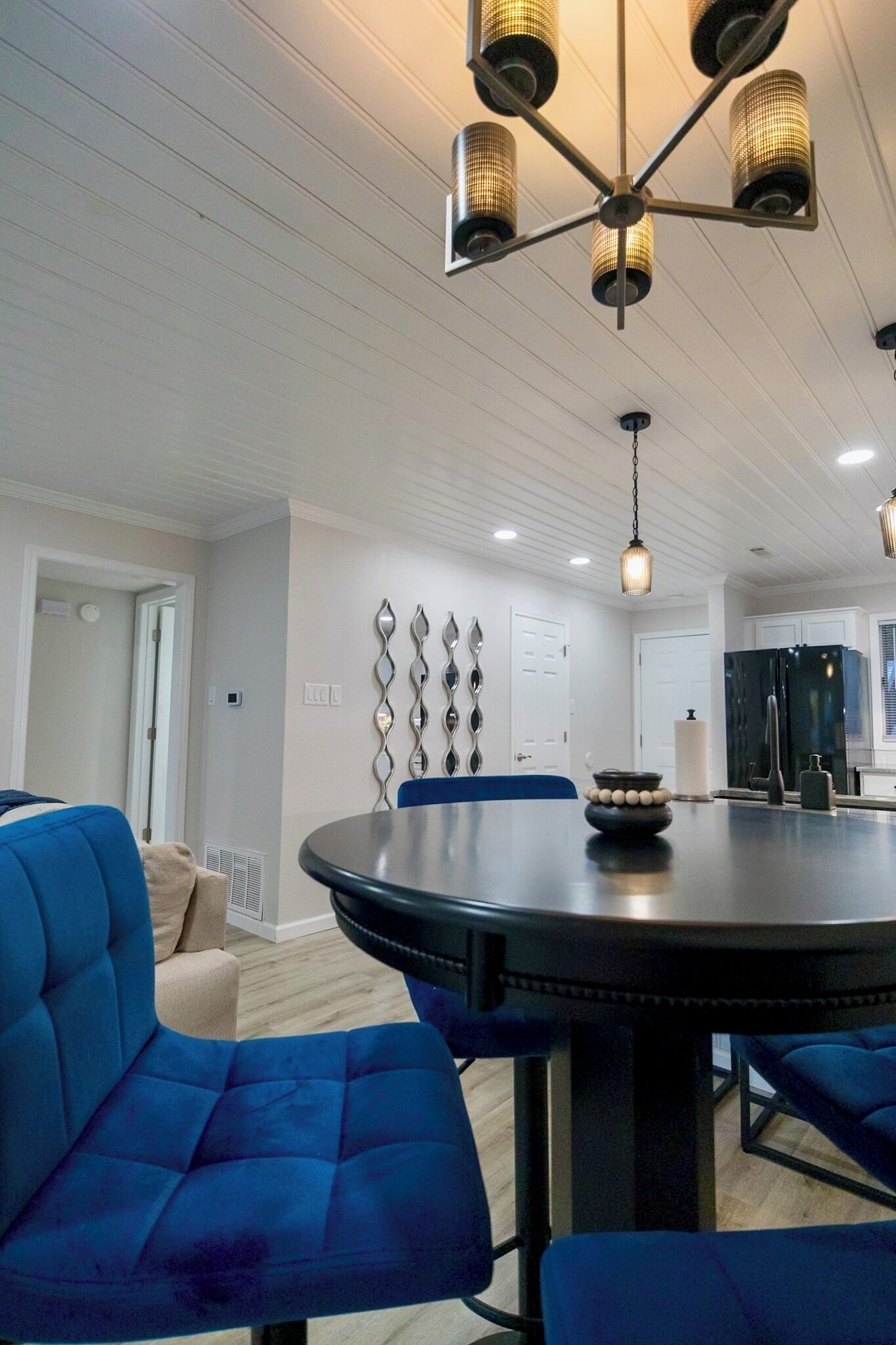 A modern dining area with a round table, blue upholstered chairs, and a chandelier.
