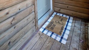 Entrada de una cabaña de madera con un letrero que dice "23C Pine Cove", una puerta y un felpudo a cuadros con el texto "Probablemente en la Playa".