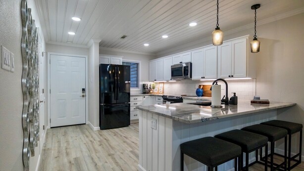 Una cocina moderna con armarios blancos, un refrigerador negro, un microondas y una isla grande con taburetes de bar.