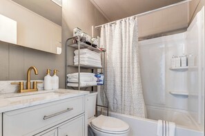 A modern bathroom with a marble sink, gold faucet, and a shelf with toiletries.