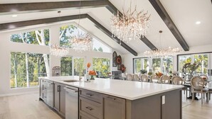 Una cocina amplia con una isla grande, modernas lámparas colgantes y grandes ventanas que ofrecen vistas al exterior.