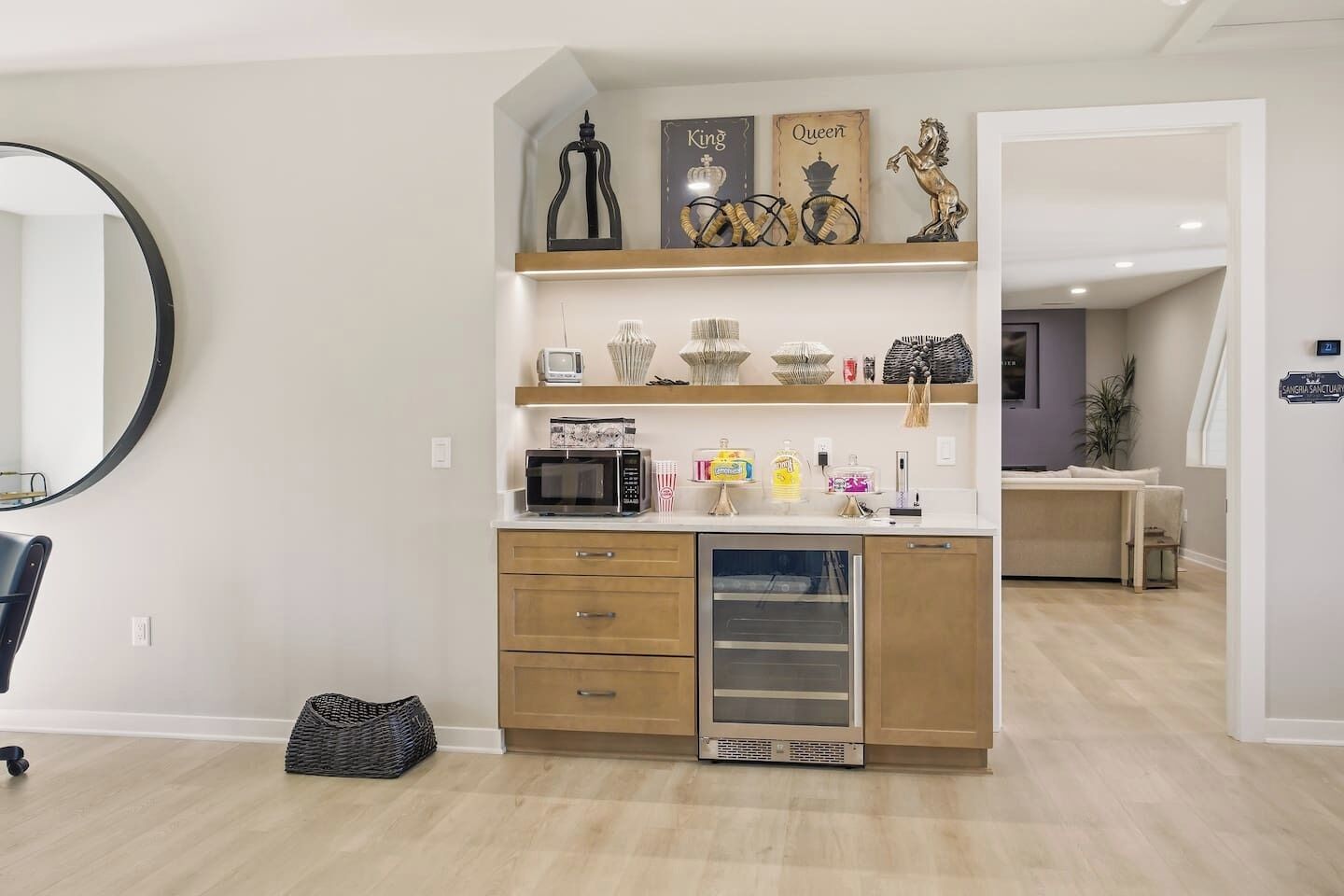 A modern kitchen with wooden cabinets, a microwave, and a built-in oven. There are decorative items on the shelves, including a sign that says "King" and "Queen."