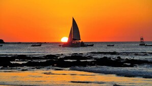 Tramonto su una spiaggia con barche e costa rocciosa.