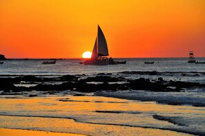 Een zonsondergang boven een strand met boten en een rotsachtige kustlijn.