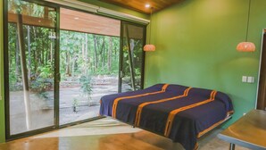 Una stanza con un letto, un tavolo e vista su una foresta attraverso ampie finestre.