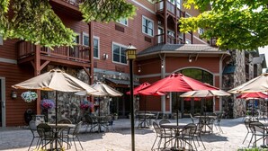 An outdoor patio area with tables and chairs, surrounded by a stone wall and a building with balconies. - Hunter Mountain 1BR Condo | Slopeside Access (Hunter)