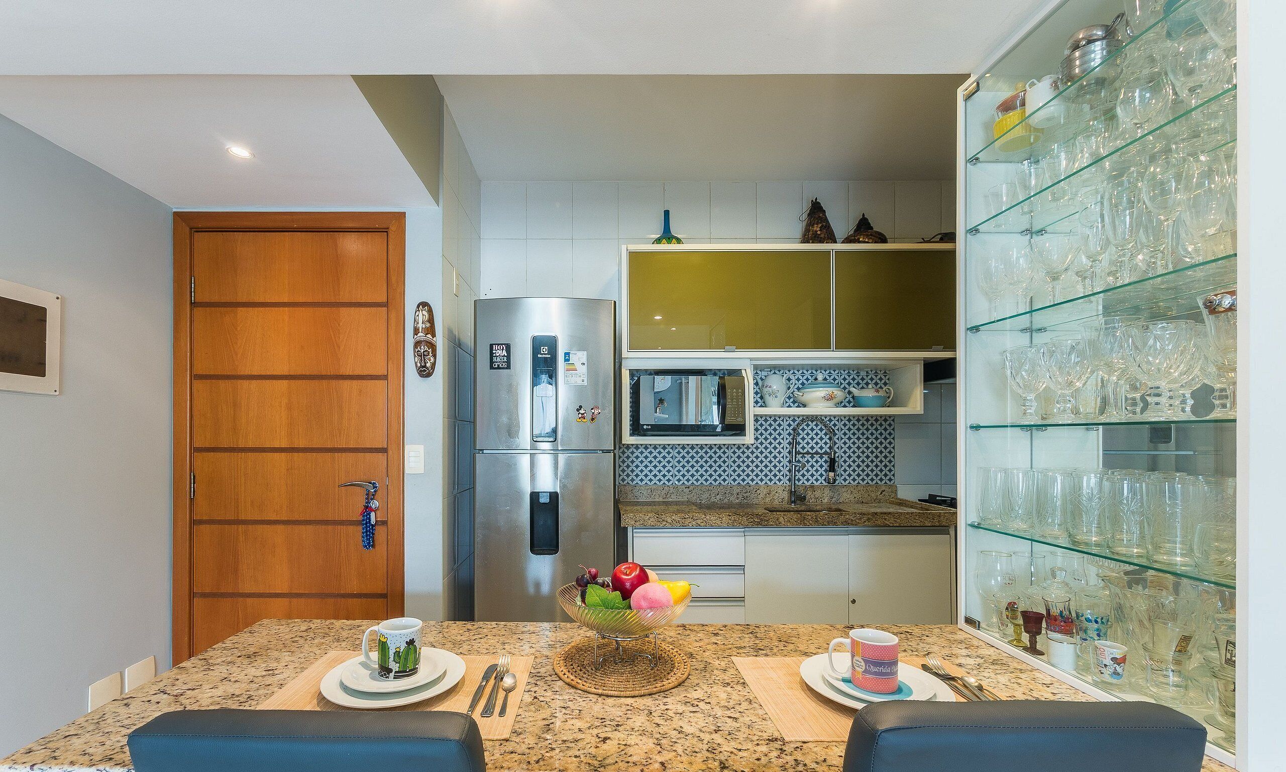 A compact kitchen with a refrigerator, microwave, and glass cabinet filled with dishes.