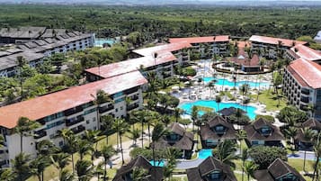 Resort com várias construções, área de piscina central e palmeiras ao redor.