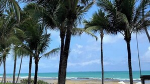 A beach view with palm trees, a pool, and a beach area with umbrellas. - Marulhos Suítes Resort (Ipojuca)