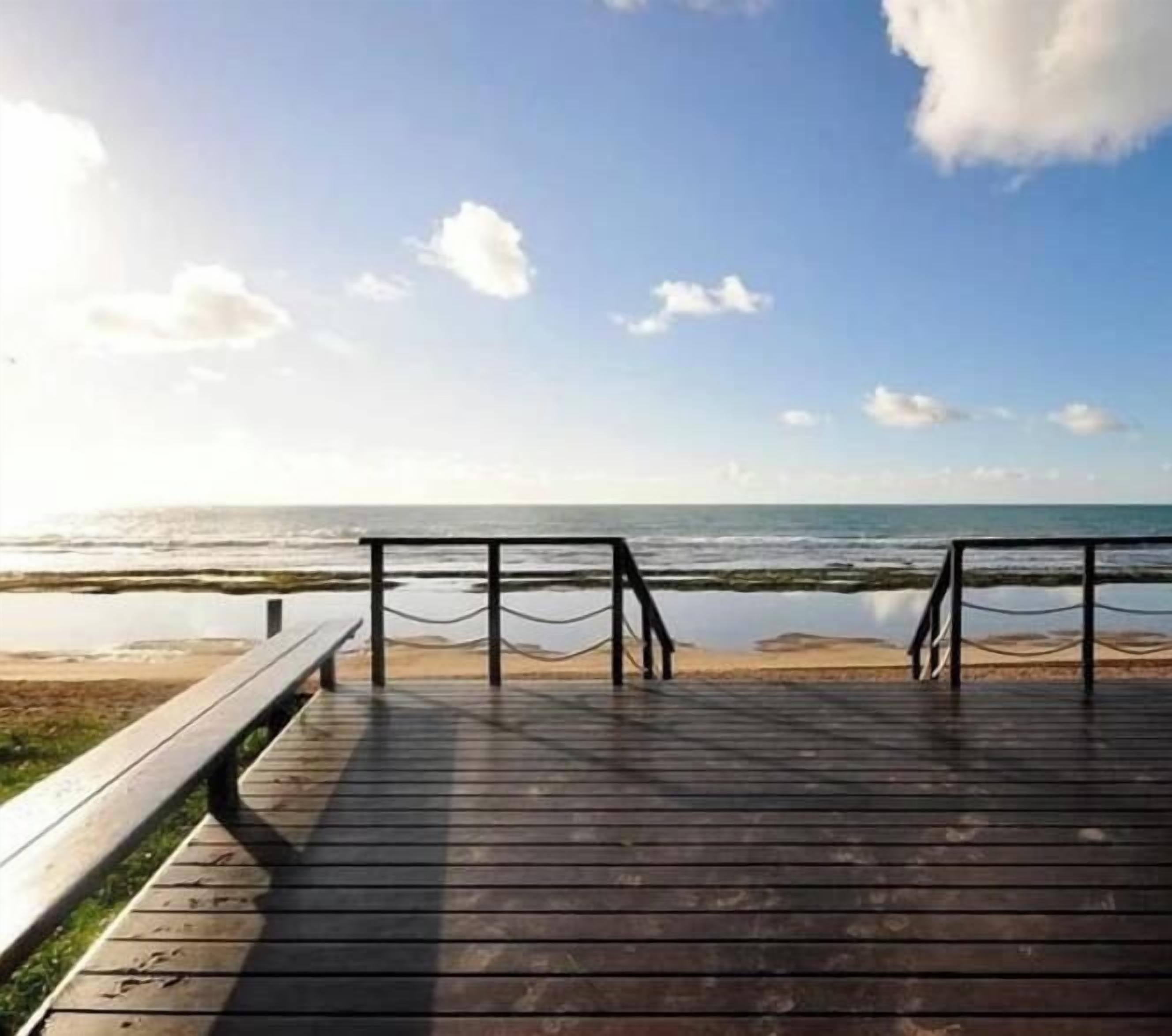 A wooden boardwalk leading to a beach with a clear sky and calm sea.