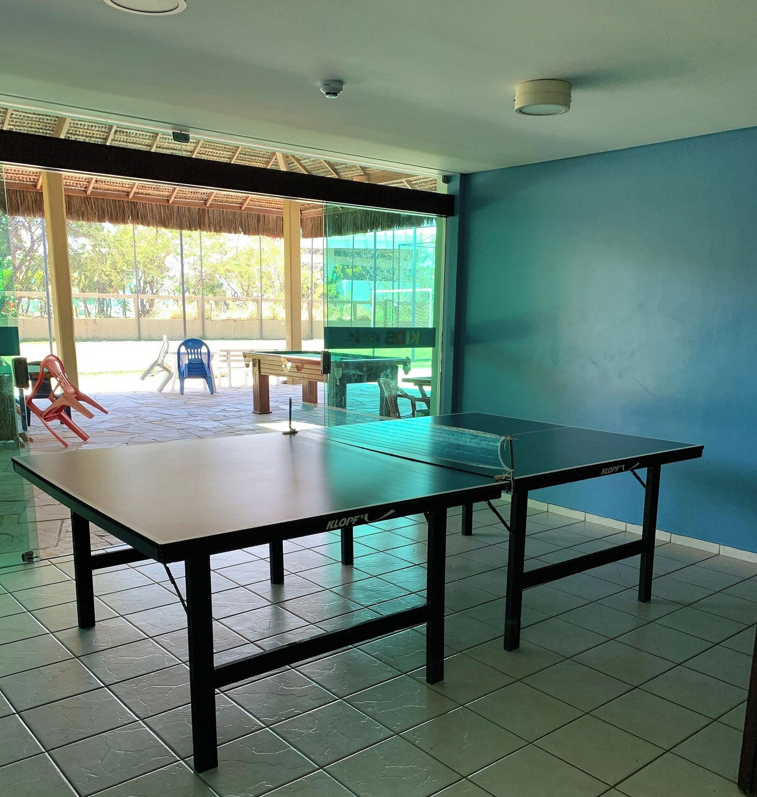 Quarto com mesa de pingue-pongue, telhado de palha e vista para o exterior.