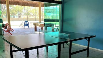 Quarto com mesa de pingue-pongue, telhado de palha e vista para o exterior.