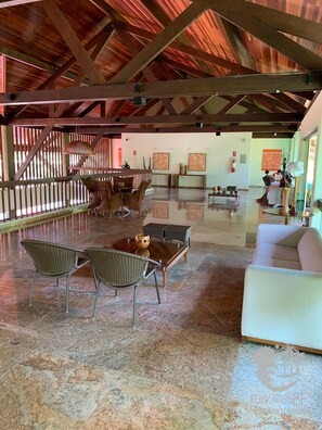 A spacious lobby with a high ceiling, wooden beams, a reception desk, seating area, and artwork on the walls. - Marulhos Suítes Resort (Ipojuca)