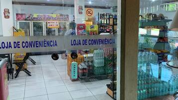 Uma loja de conveniência com fachada de vidro transparente, diversos produtos nas prateleiras e um letreiro indicando que é uma 'LOJA DE CONVENIÊNCIA'.