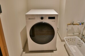 Eine Waschmaschine mit Frontöffnung in einem Waschraum, in der Nähe ein weißer Wäschekorb steht.