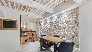 Un coin repas avec une table en bois et des chaises noires, un mur en pierre et un escalier menant à une autre pièce.