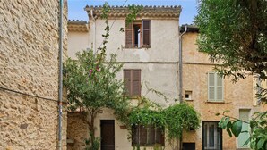 Une cour avec un mur en pierre, un bâtiment doté d’une porte et de fenêtres, et un arbre en fleurs.