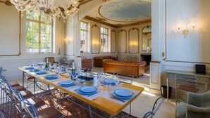 Une salle à manger avec une longue table dressée pour le repas, un lustre et une vue sur le jardin grâce à de grandes fenêtres.
