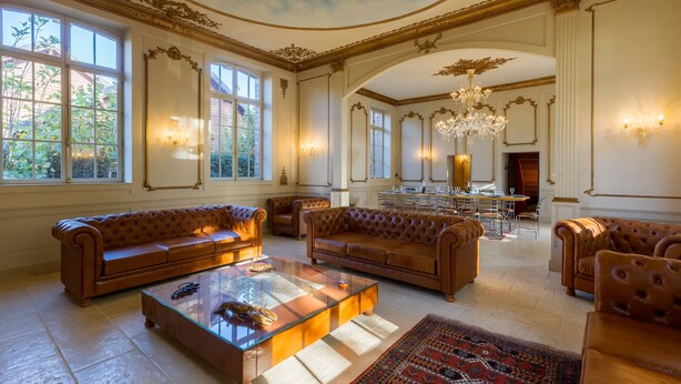 Un salon spacieux avec des canapés en cuir, une table basse en verre et un lustre.
