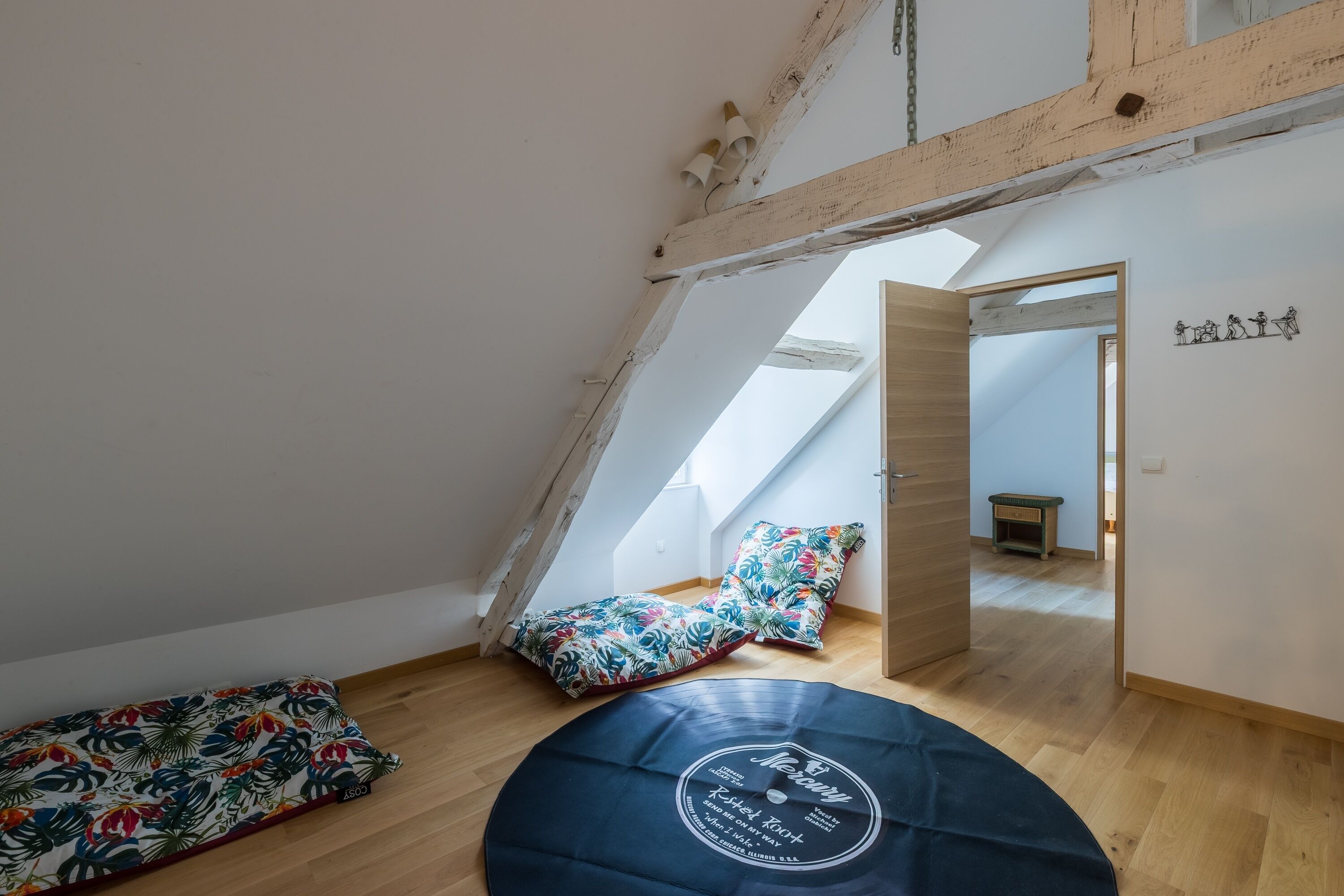 Una habitación acogedora en el ático, con techo inclinado, un sofá de vinilo estampado con motivos florales, un disco de vinilo y una pequeña mesa de madera.