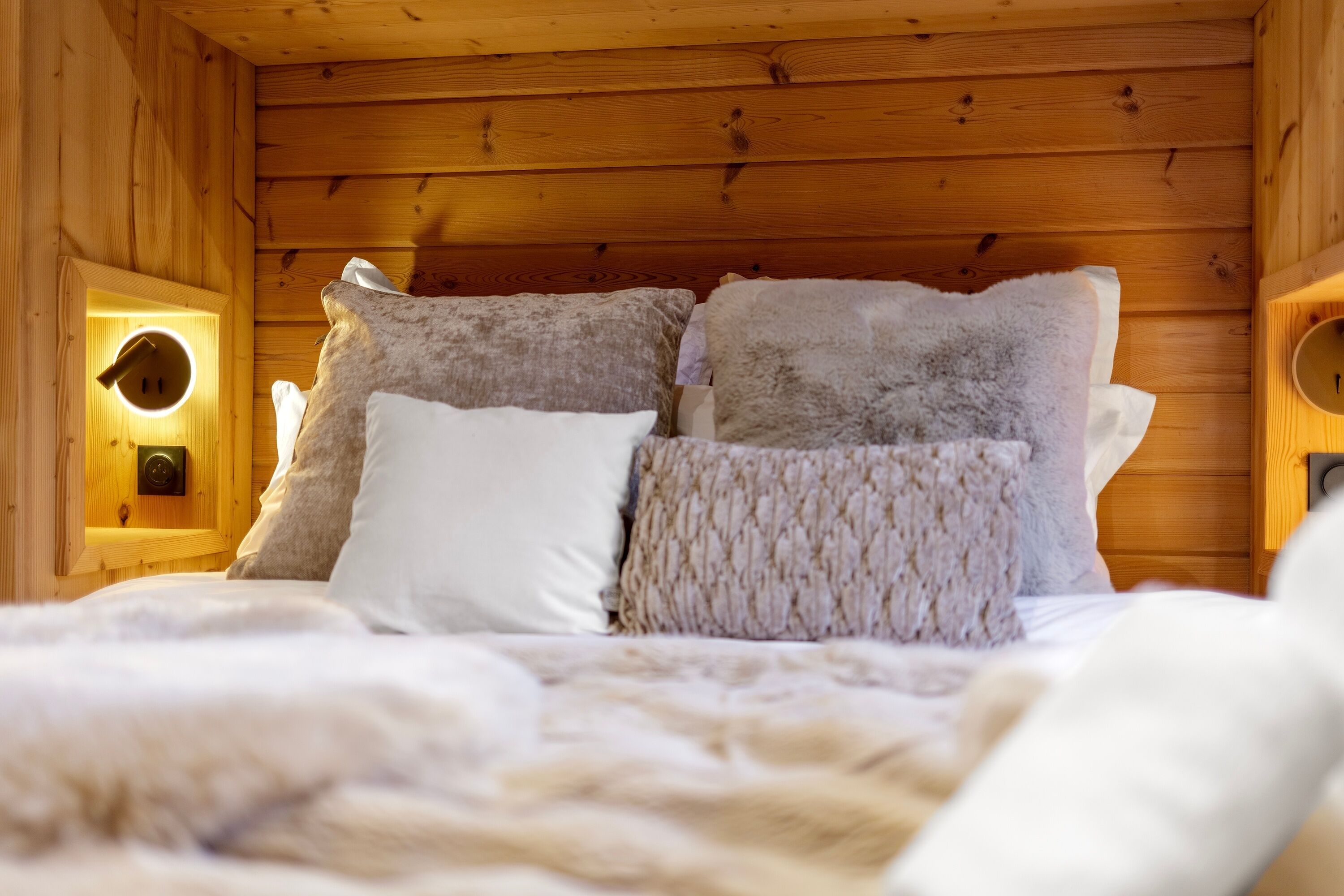 Un dormitorio rústico de madera con una cama, almohadillas mullidas y una lámpara fijada a la pared.