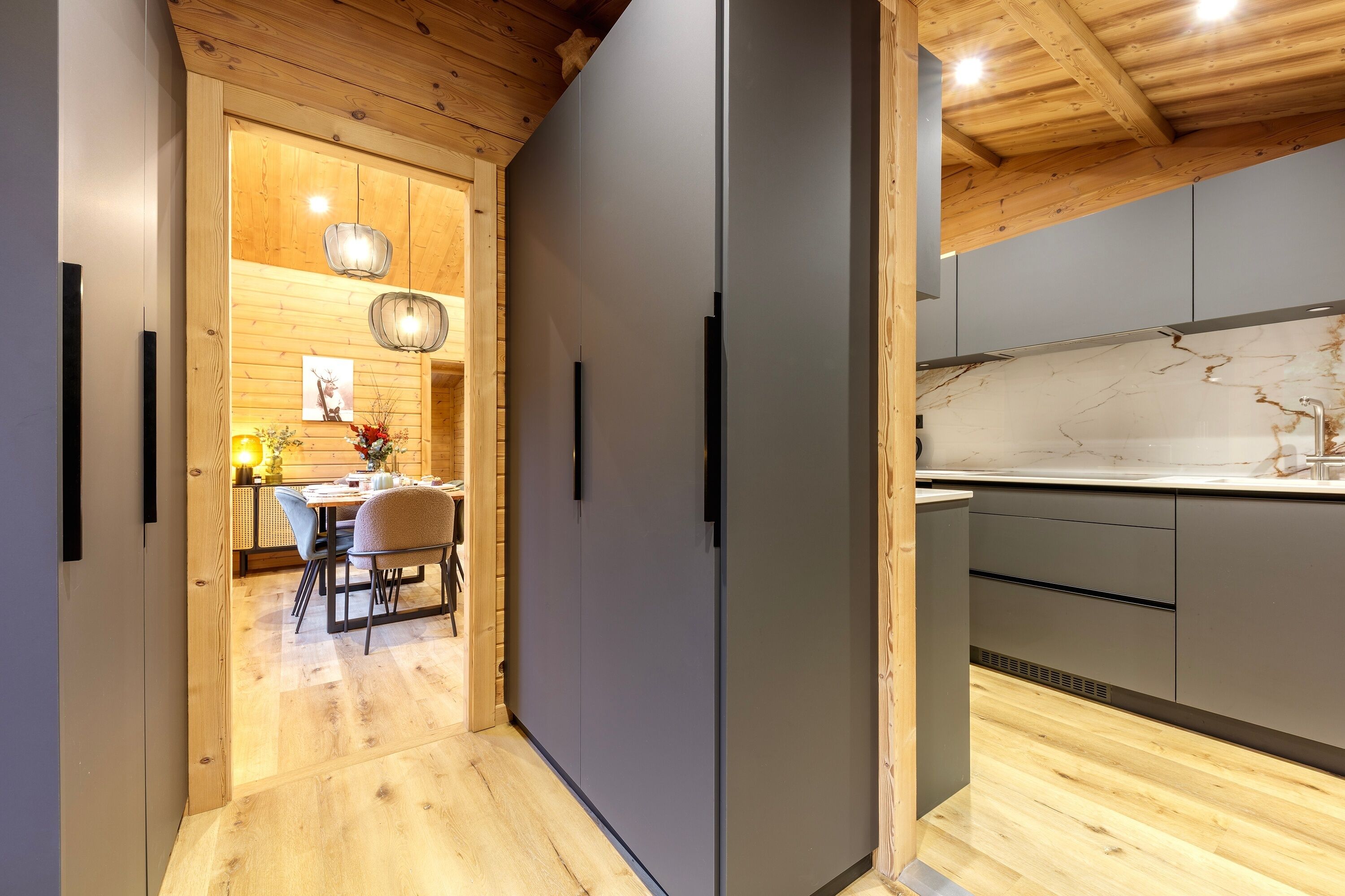 A modern kitchen with grey cabinets, a wooden ceiling, and a dining area with a table and chairs.