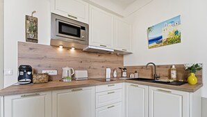 A modern kitchen with white cabinetry, a wooden countertop, a microwave, a toaster, and a sink. - L'Azur Antibois – Charme & confort dans le Vieil Antibes (Antibes)