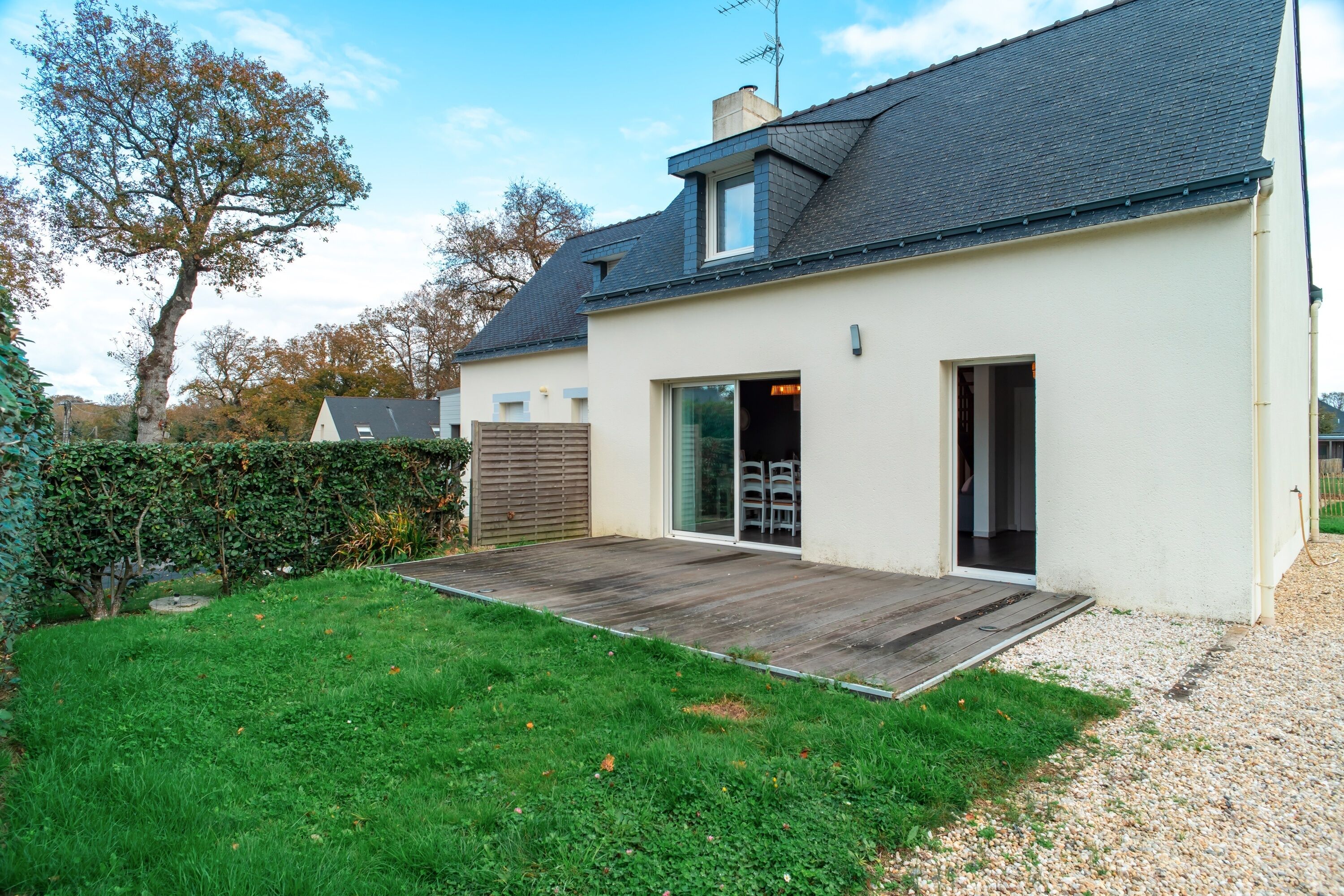 Et moderne hus med træterrasse, garage og et stort træ i haven.