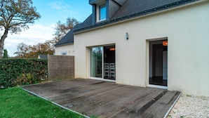 Een modern huis met een houten terras, grote schuifpuien en een kleine aanleun garage.