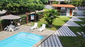 A swimming pool with lounge chairs, a small building, and surrounding greenery. - Condomínio Merepe Residence (Ipojuca)