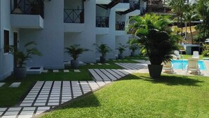 A multi-story hotel with balconies, a swimming pool, and a well-maintained lawn. - Condomínio Merepe Residence (Ipojuca)