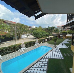 Una piscina con sillas de descanso y sombrillas, rodeada de vegetación y edificios.