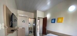 Una habitación de hotel con una cama, televisor, baño y una puerta que da a otra habitación.
