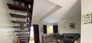 Una sala de estar con escaleras, un sofá, una mesa de centro y una ventana con persianas.