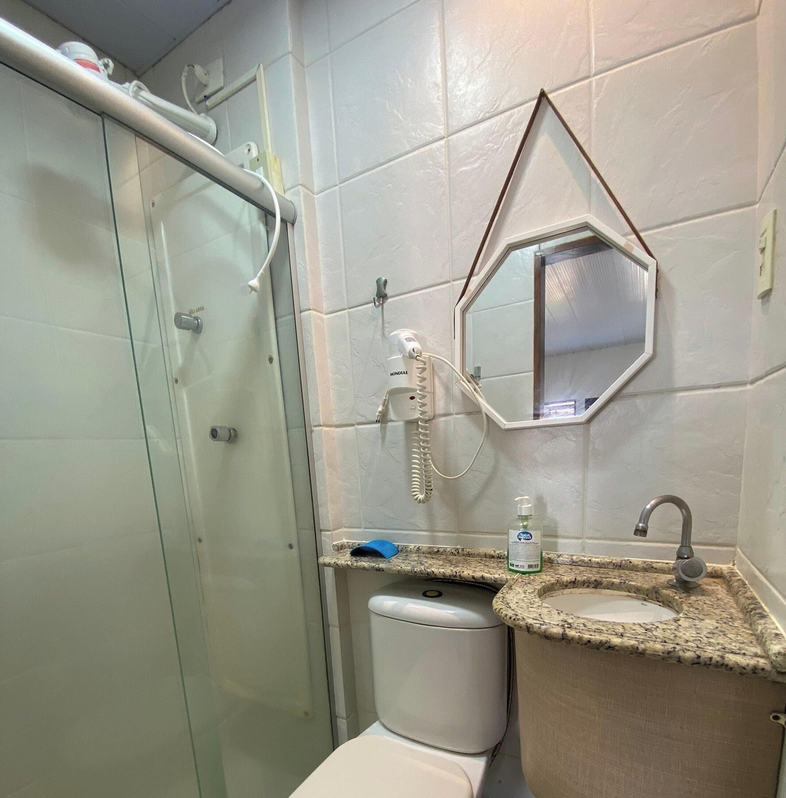 Un bagno con cabina doccia in vetro, un water, un lavabo con piano in granito e uno specchio.