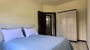 Ein Schlafzimmer mit Bett, Kleiderschrank und angrenzendem Badezimmer, das durch eine offene Tür sichtbar ist.