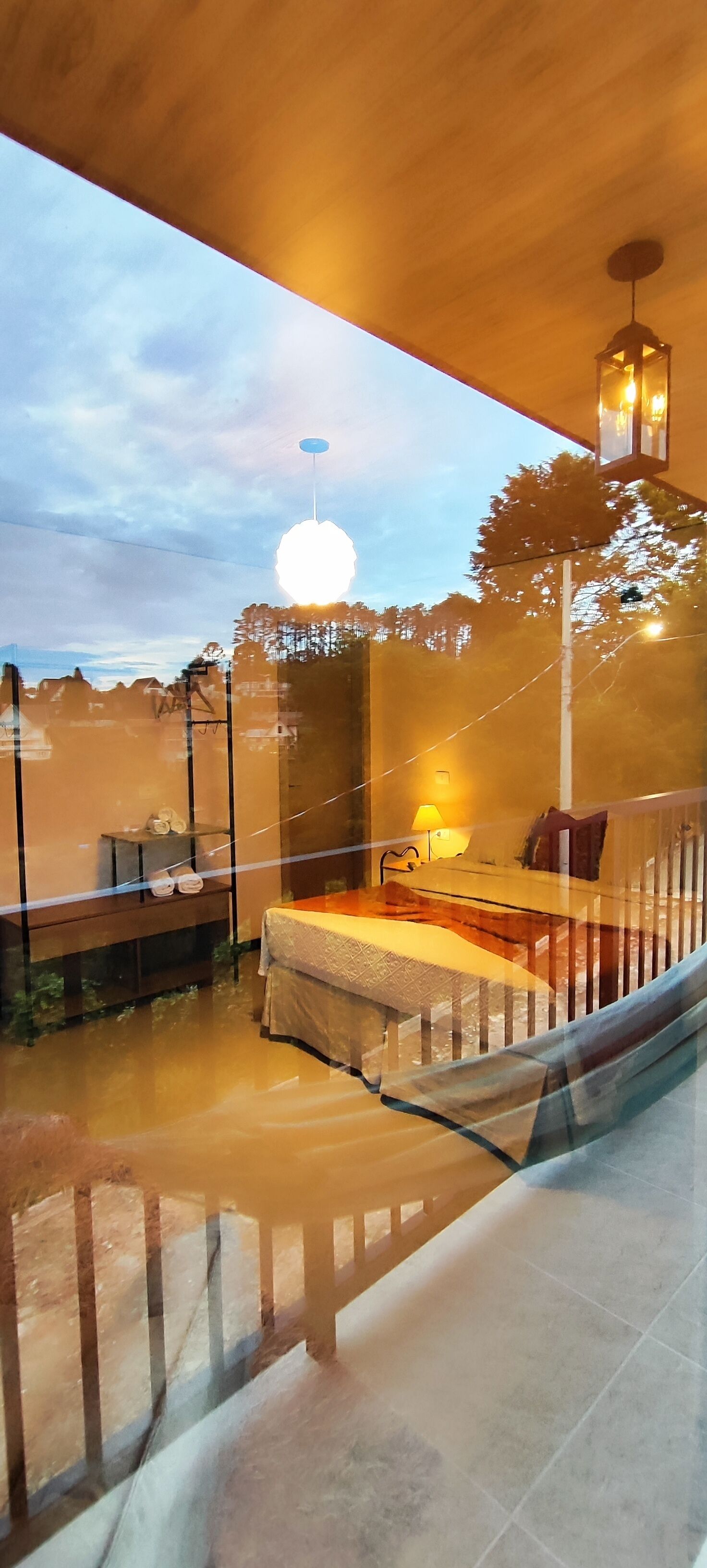 Ein modernes Interieur mit Glastrennwand, einem Bett mit weißer Bettdecke, einer Lampe und einer Pendelleuchte.