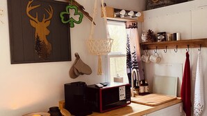 A kitchen with a wooden countertop, white cabinets, a hanging macrame light, a deer silhouette artwork, and a coffee maker.