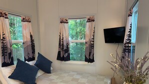A cozy room with a bed, a TV mounted on the wall, and a window with curtains.