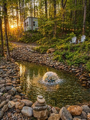 A serene pond with a stone border, surrounded by lush greenery and trees. - Romantic Tiny Cabin with Private Hot Tub in the Smoky Mountain Woods (Del Rio)